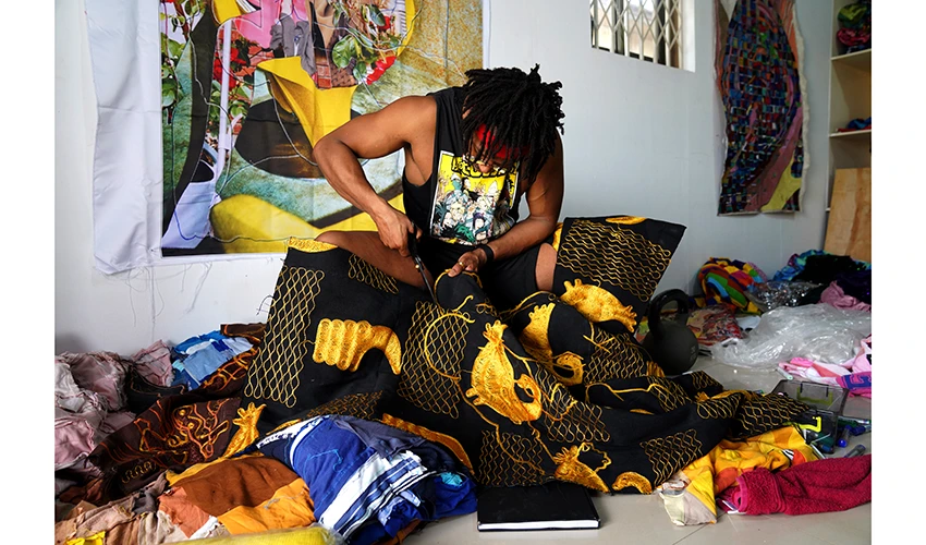photo of a seated Black man in a dark cutoff tee cutting ornate fabric